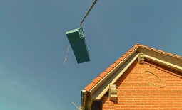 Ein an einem Kran befestigter PVC-Pool wird über ein Hausdach gehoben.