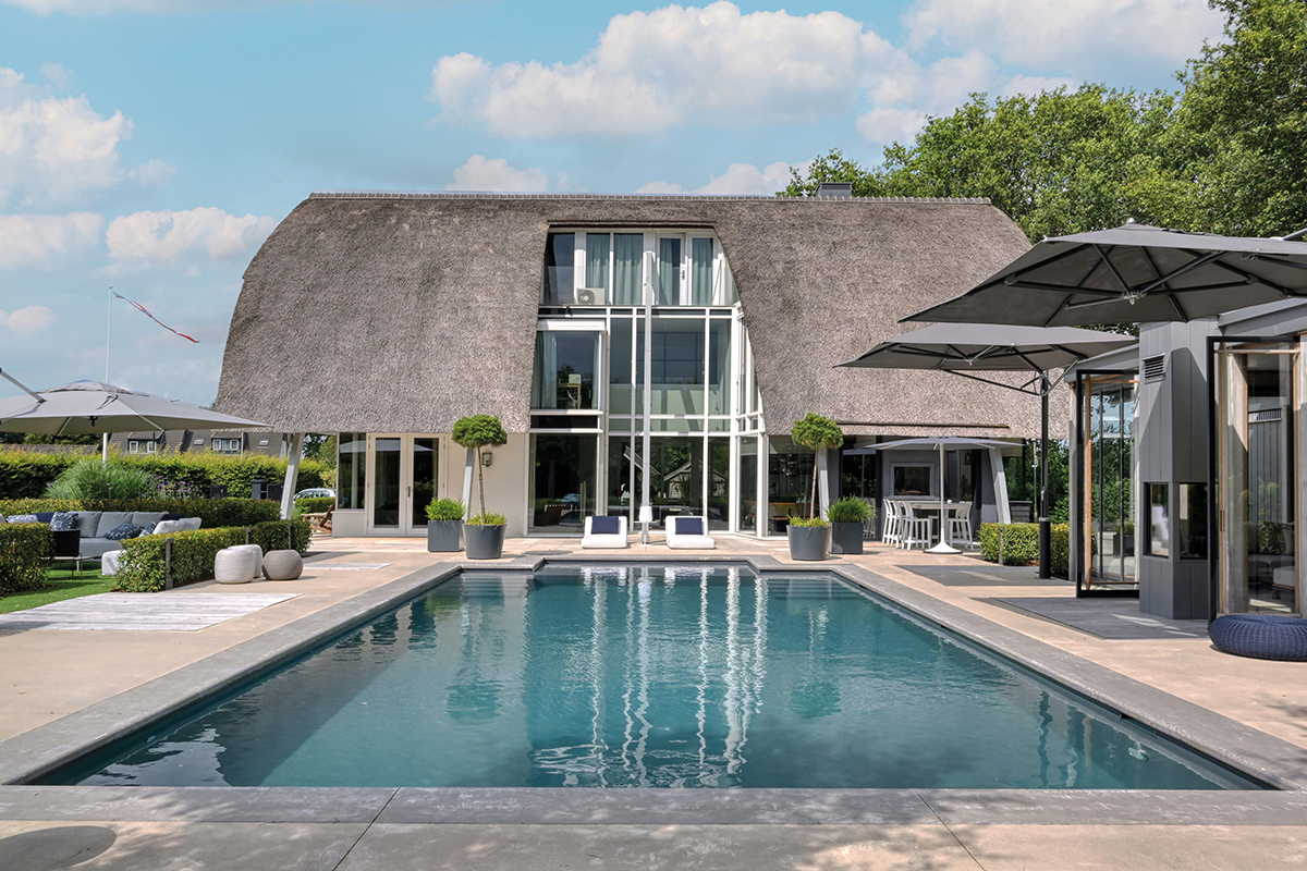 Ein Pool vor einem großen Wohnhaus mit Reetdach.
