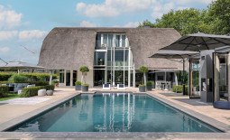 Ein Pool vor einem großen Wohnhaus mit Reetdach.