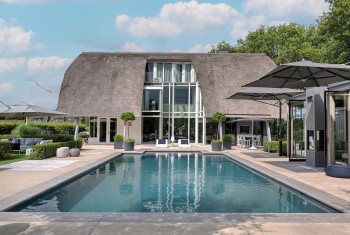 Ein Pool vor einem großen Wohnhaus mit Reetdach.