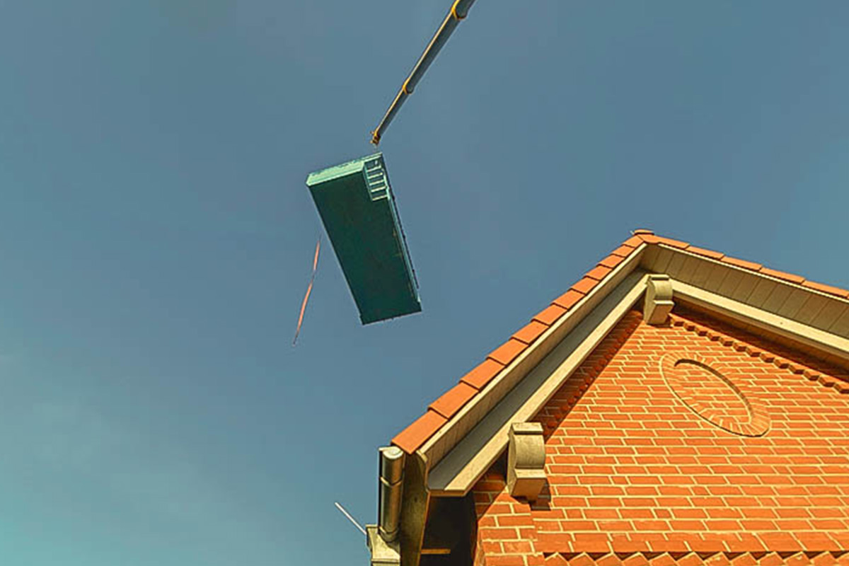 Ein an einem Kran befestigter PVC-Pool wird über ein Hausdach gehoben.